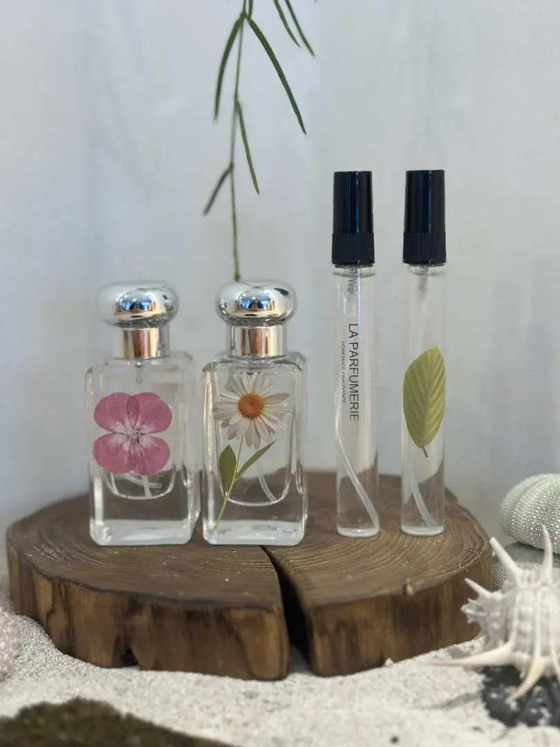 Jeju Island perfume making experience results, featuring two dried flower-infused perfumes and sample sprays, placed on a wooden base with beach shells, creating a natural island ambiance.