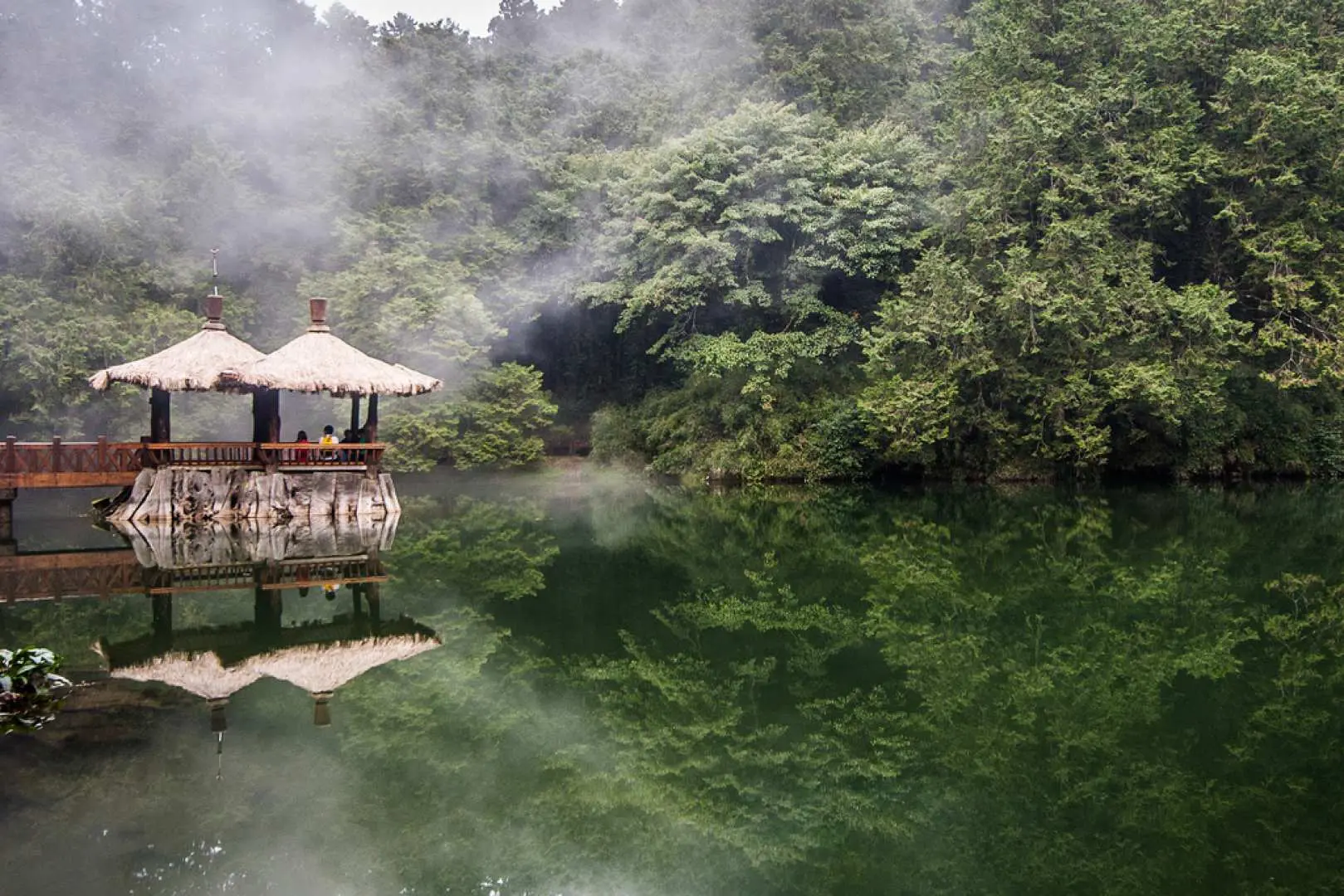 阿里山姊妹潭在薄霧籠罩下，木造涼亭與橋樑倒影更顯朦朧詩意，呈現如夢似幻的森林湖泊景緻。
