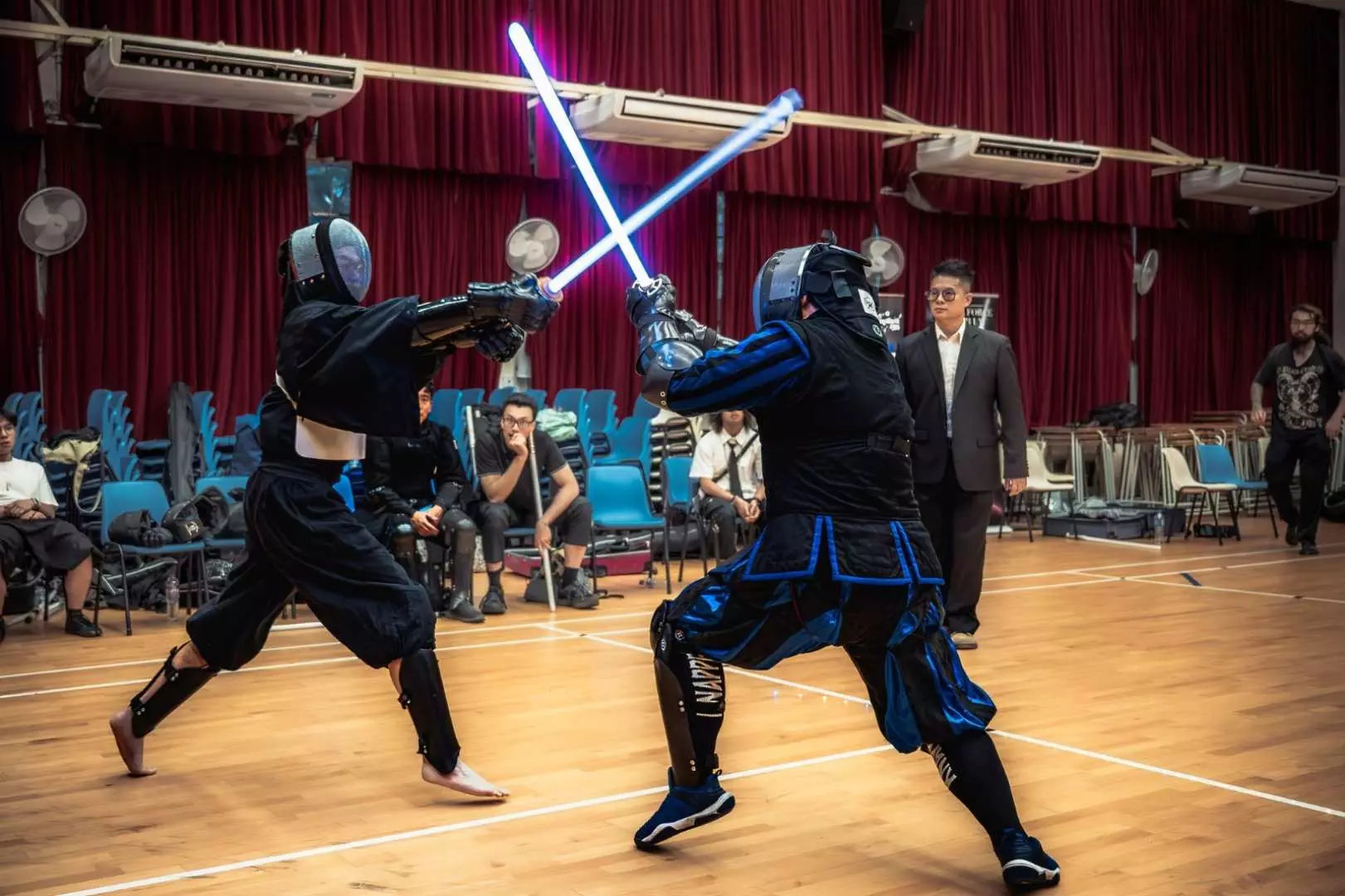 Two participants in full protective gear engage in an intense lightsaber duel at Starblade Hong Kong, with glowing blue lightsabers clashing, showcasing thrilling combat.