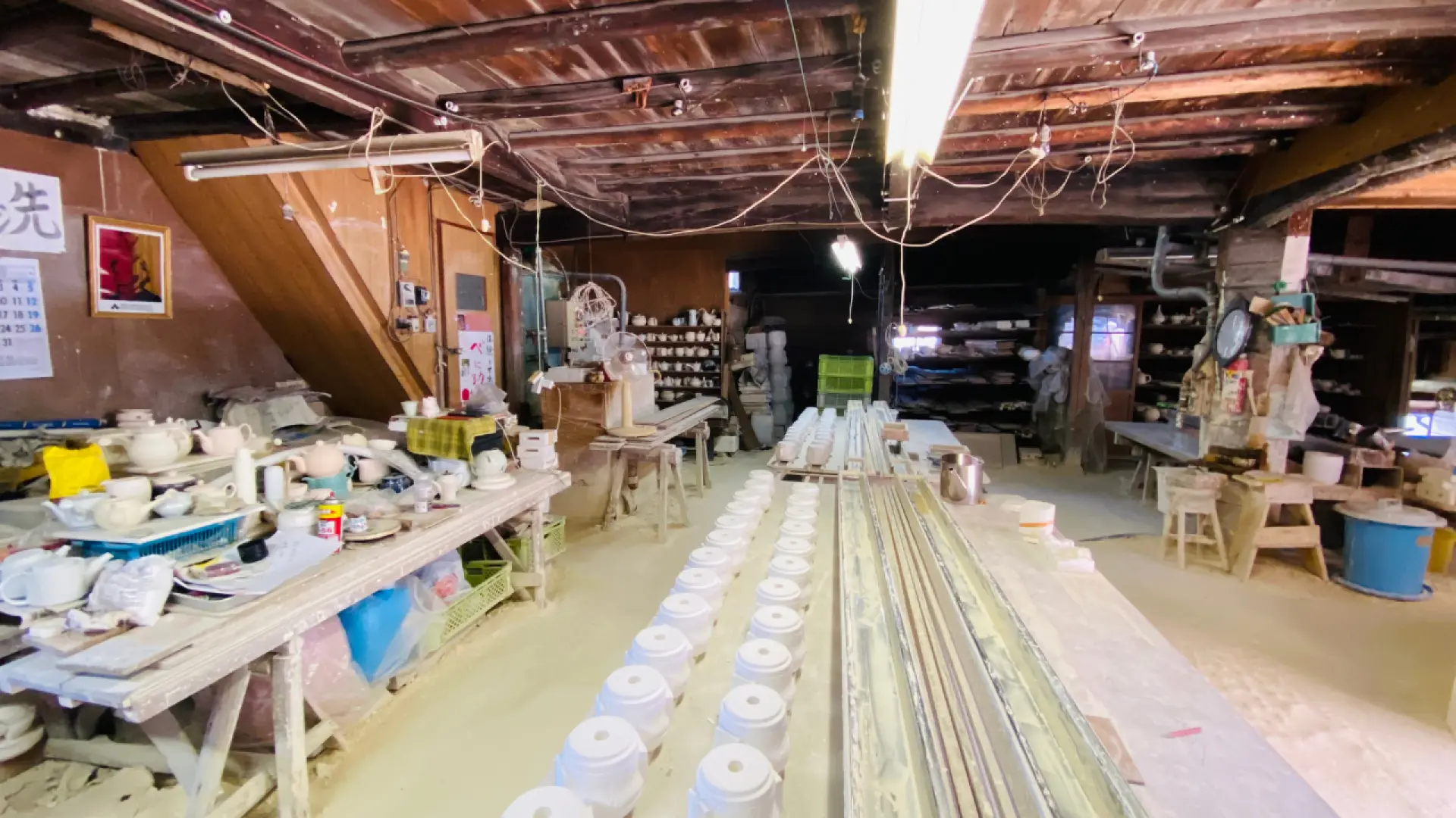 長崎波佐見燒傳統陶藝工作室內部全景，展示工作區、工具和眾多未完成的陶瓷作品，充滿歷史氣息。