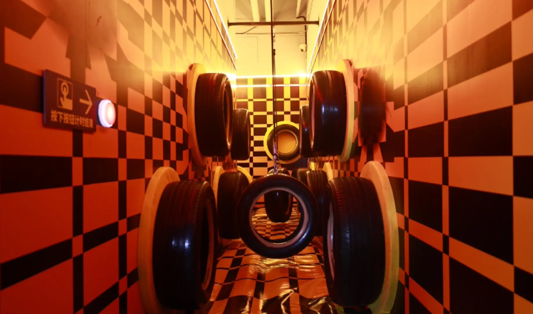 Shenzhen Airpai Sports Carnival's installation art corridor with optical illusions, featuring orange and black checkerboard walls and floating tires, creating a unique futuristic tech aesthetic.