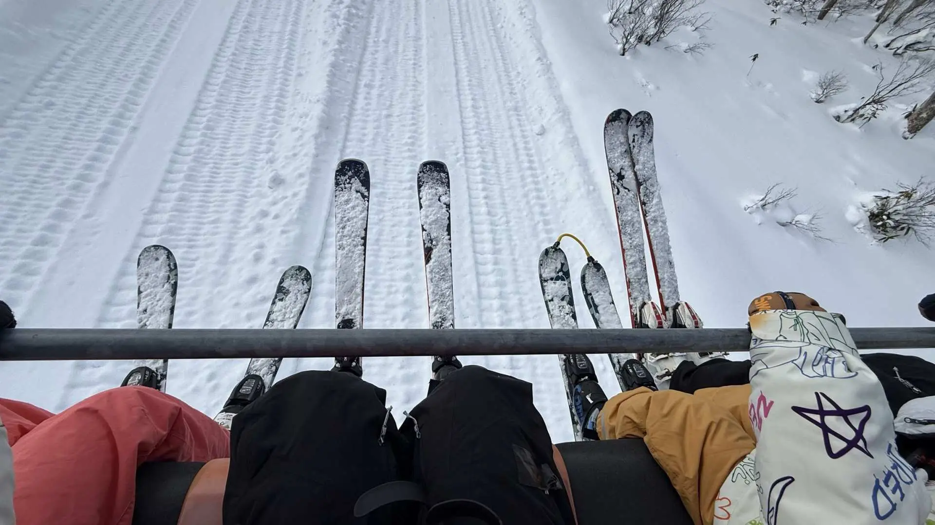 A view from the Niseko ski lift, overlooking wide slopes with clear ski tracks below, showcasing the freedom and joy of exploring Hokkaido's ski fields, with close-ups of skis and ski pants.