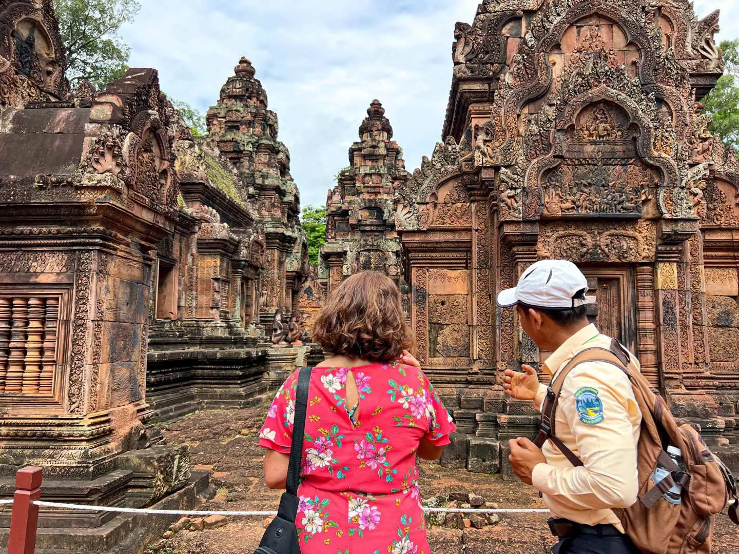 Tourist with guide exploring the intricately carved red sandstone temples of Banteay Srei in Siem Reap, Cambodia, highlighting ancient Khmer artistry.