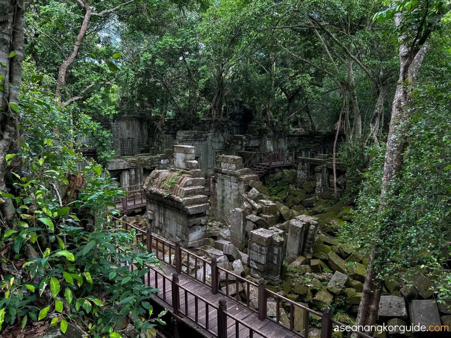 Exploring the atmospheric jungle-covered ruins of Beng Mealea temple in Cambodia, with wooden walkways guiding visitors through the ancient collapsed structures.