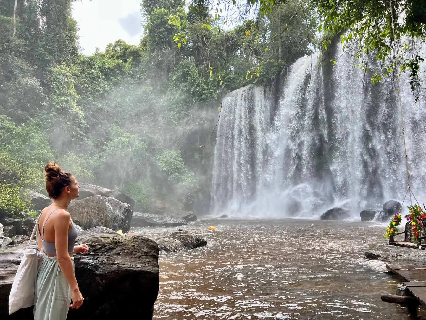 Visitor admiring the impressive waterfall at Phnom Kulen in Cambodia, surrounded by lush tropical greenery, perfect for nature exploration.