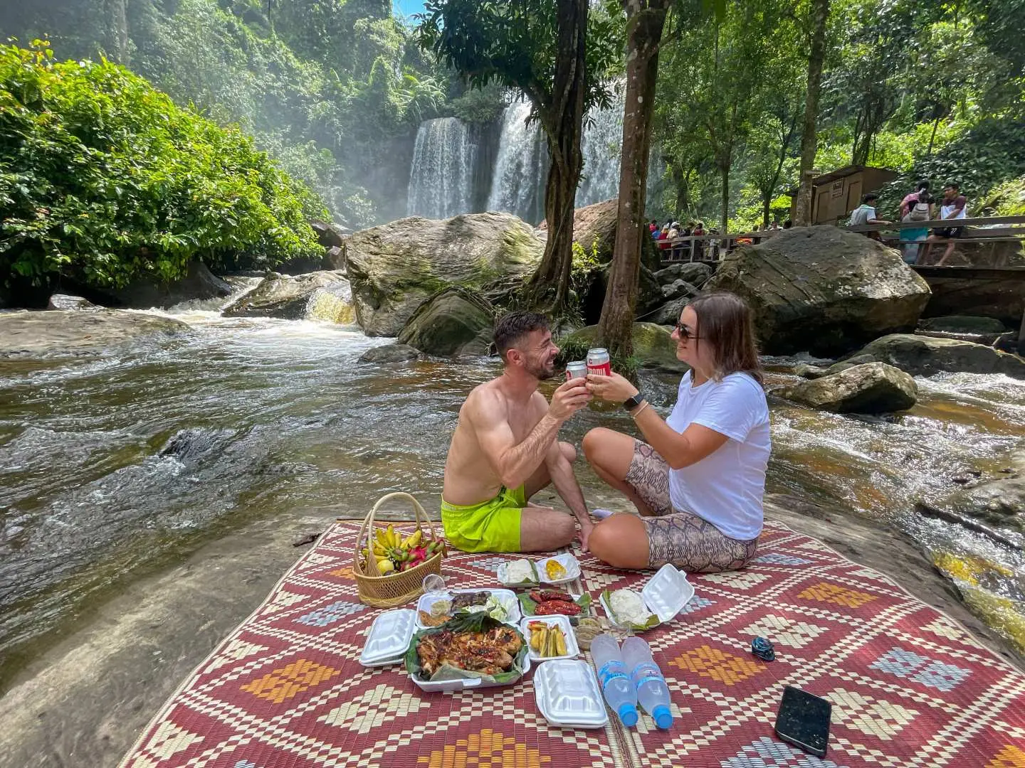 Couple enjoying a delightful picnic lunch by the waterfall at Phnom Kulen, Cambodia, amidst stunning natural surroundings.