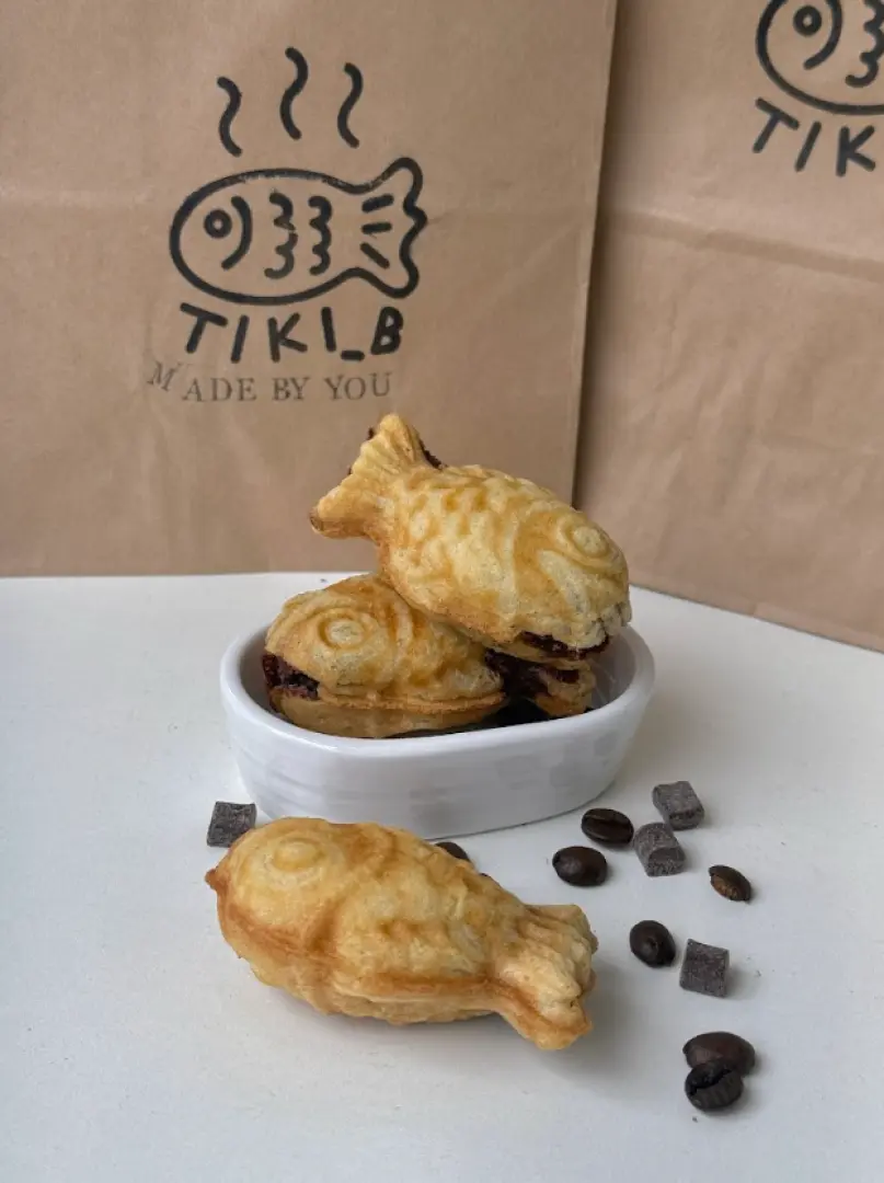 Finished Bungeoppang from the Seoul Korean snack making experience, golden crispy fish-shaped pastries with chocolate filling, displayed in a white bowl with branded bags in the background.