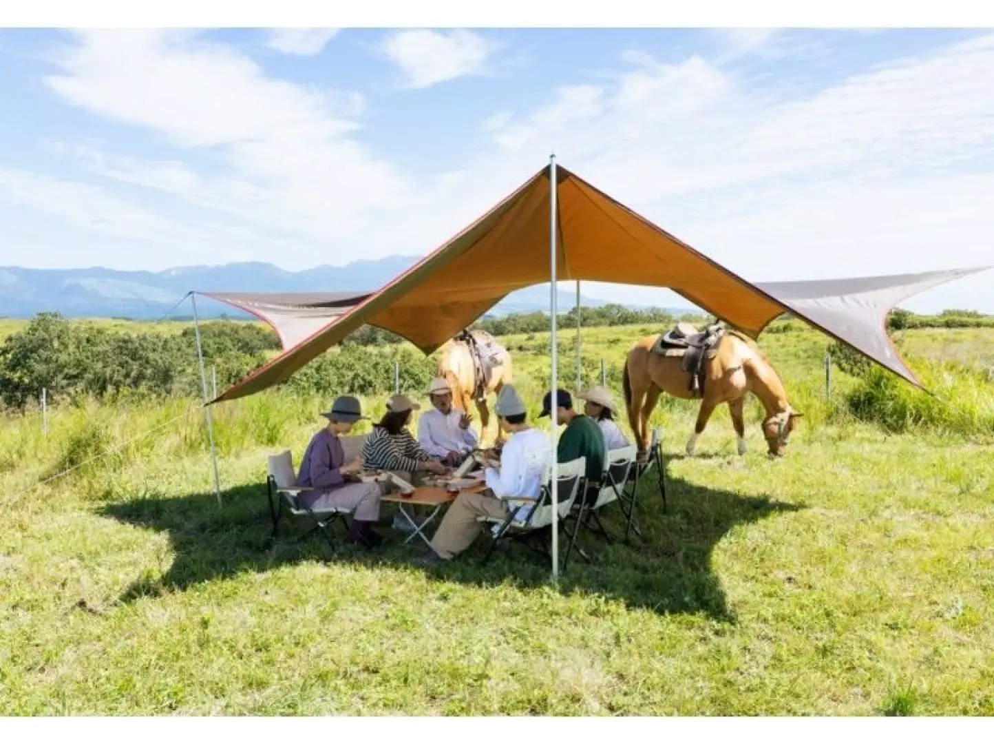 A wider view of visitors and local farmers having a peaceful picnic lunch under a tent, surrounded by the stunning vastness of Aso's Thousand-Year Grassland in Kumamoto, Japan.