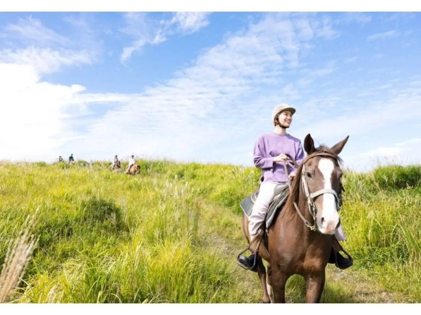 A joyous traveler on horseback explores the expansive Aso Thousand-Year Grassland in Kumamoto under a clear sky, experiencing an authentic and refreshing outdoor adventure.