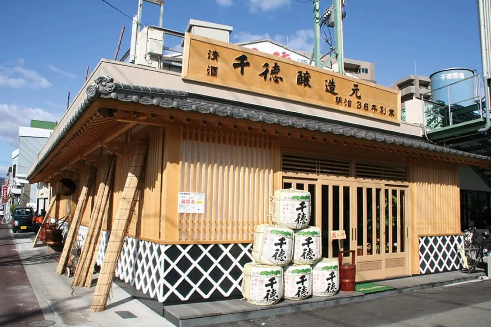 宮崎延岡仙德酒造的傳統木造建築外觀，入口處堆疊著多個印有品牌名的清酒桶，展現百年酒廠風貌。