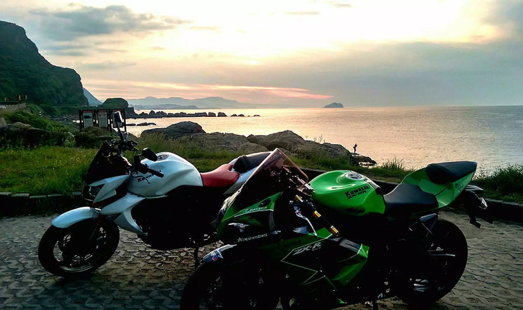 Two heavy motorcycles parked by the coast as the sunset glow illuminates the sea, with distant islands and mountains forming the unique scenery along Taipei's Pingxi line.