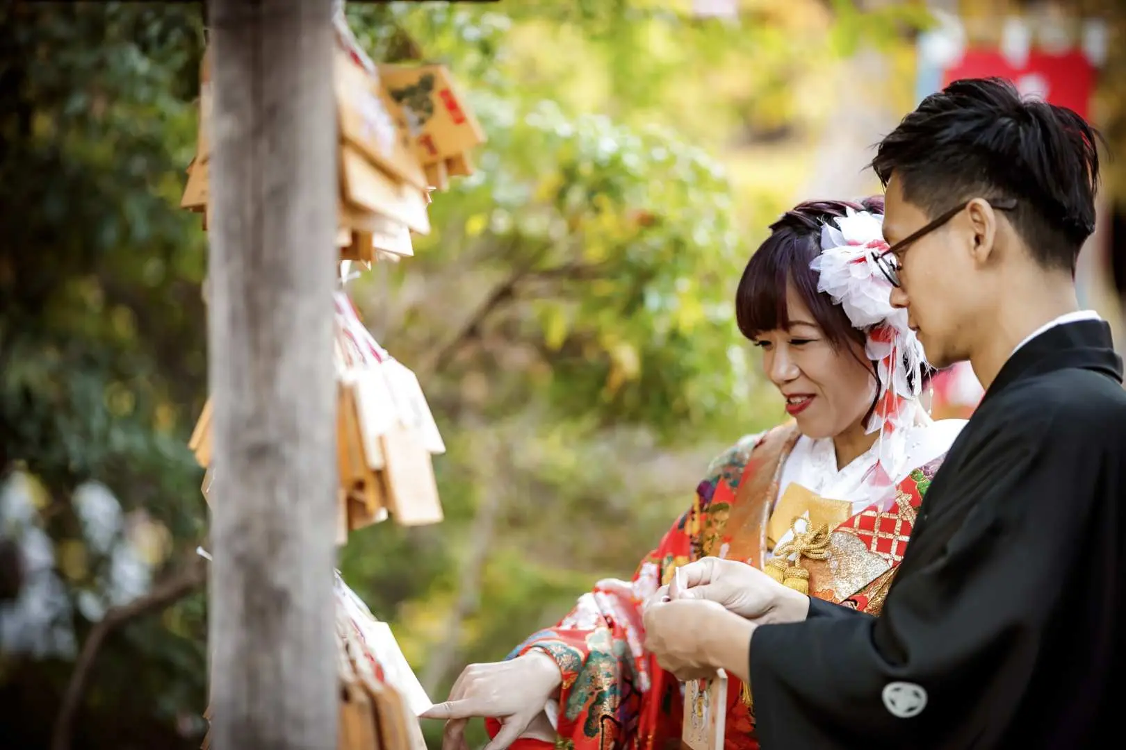 คู่บ่าวสาวชื่นชมเอมะ (ป้ายอธิษฐาน) ที่เต็มไปด้วยคำอธิษฐานระหว่างงานแต่งงานศาลเจ้าญี่ปุ่นที่โตเกียว ดื่มด่ำกับบรรยากาศของวัฒนธรรมญี่ปุ่นแบบดั้งเดิม