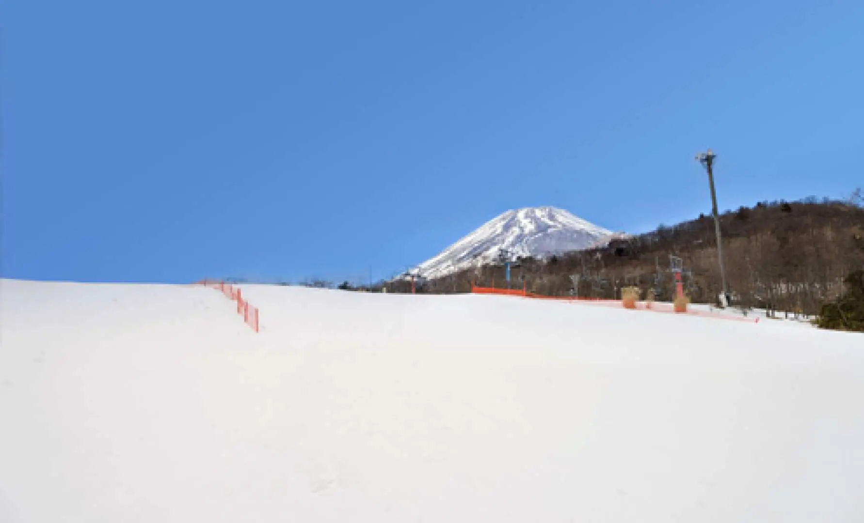 富士山Yeti滑雪场广阔的雪道，远处可见雪山峰峦，安全围栏保障滑雪者，晴空万里。