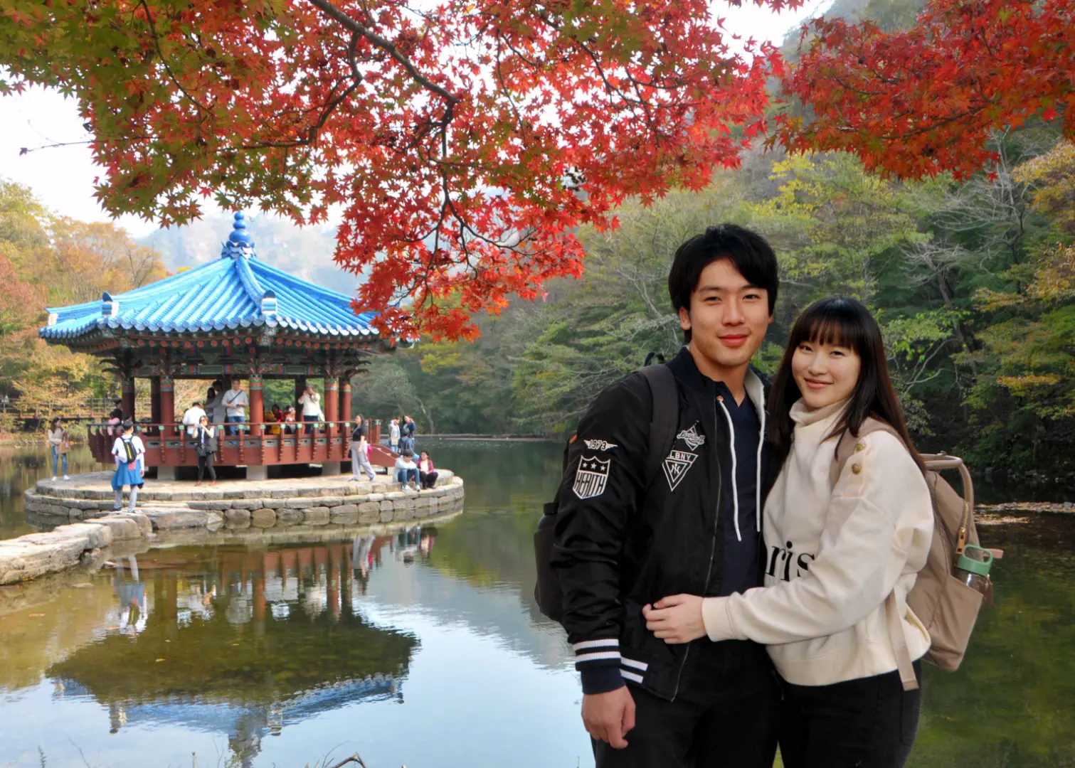 A couple enjoys an exclusive photography tour at historical sites like Gyeongbokgung Palace in Korea, admiring autumn leaves by a traditional pavilion and tranquil pond.