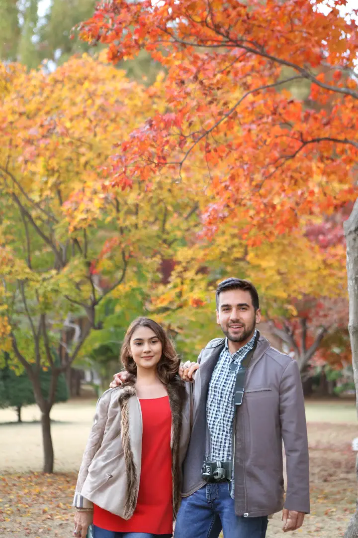 A couple takes a photo under multi-layered autumn foliage of yellow, orange, and red in Korea, showcasing the rich scenery and comfortable experience of this exclusive photography tour.