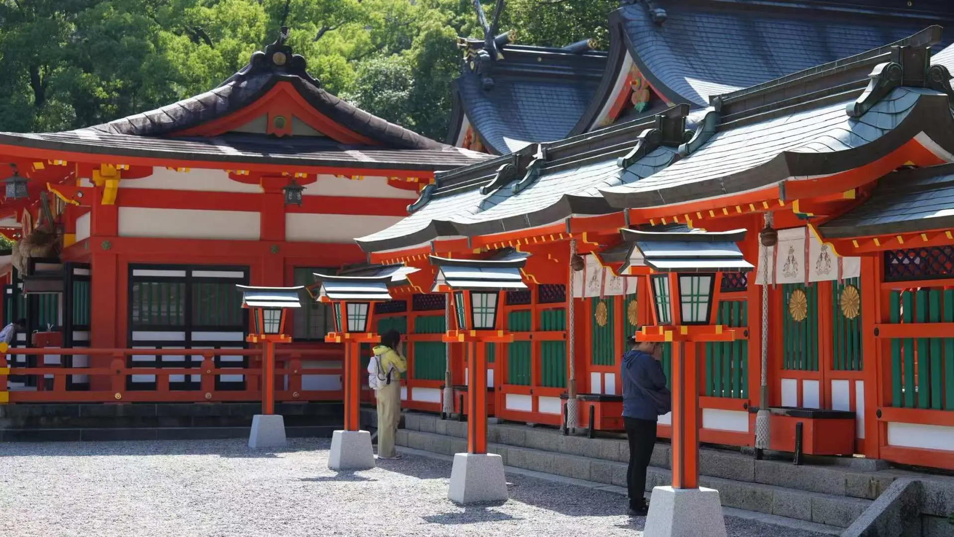 A serene courtyard within a shrine along the Kumano Kodo, featuring rows of traditional stone lanterns leading to vibrant red shrine buildings, creating an ancient and spiritual ambiance.