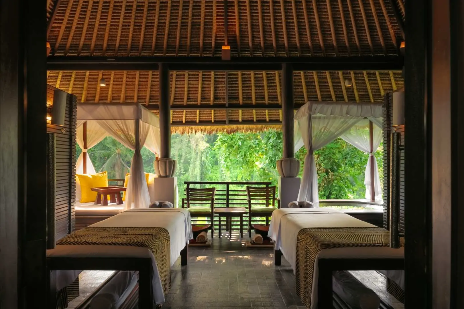 Open-air treatment room at Maya Ubud Spa, featuring two comfortable massage beds overlooking Bali's lush rainforest, offering a serene and relaxing experience.