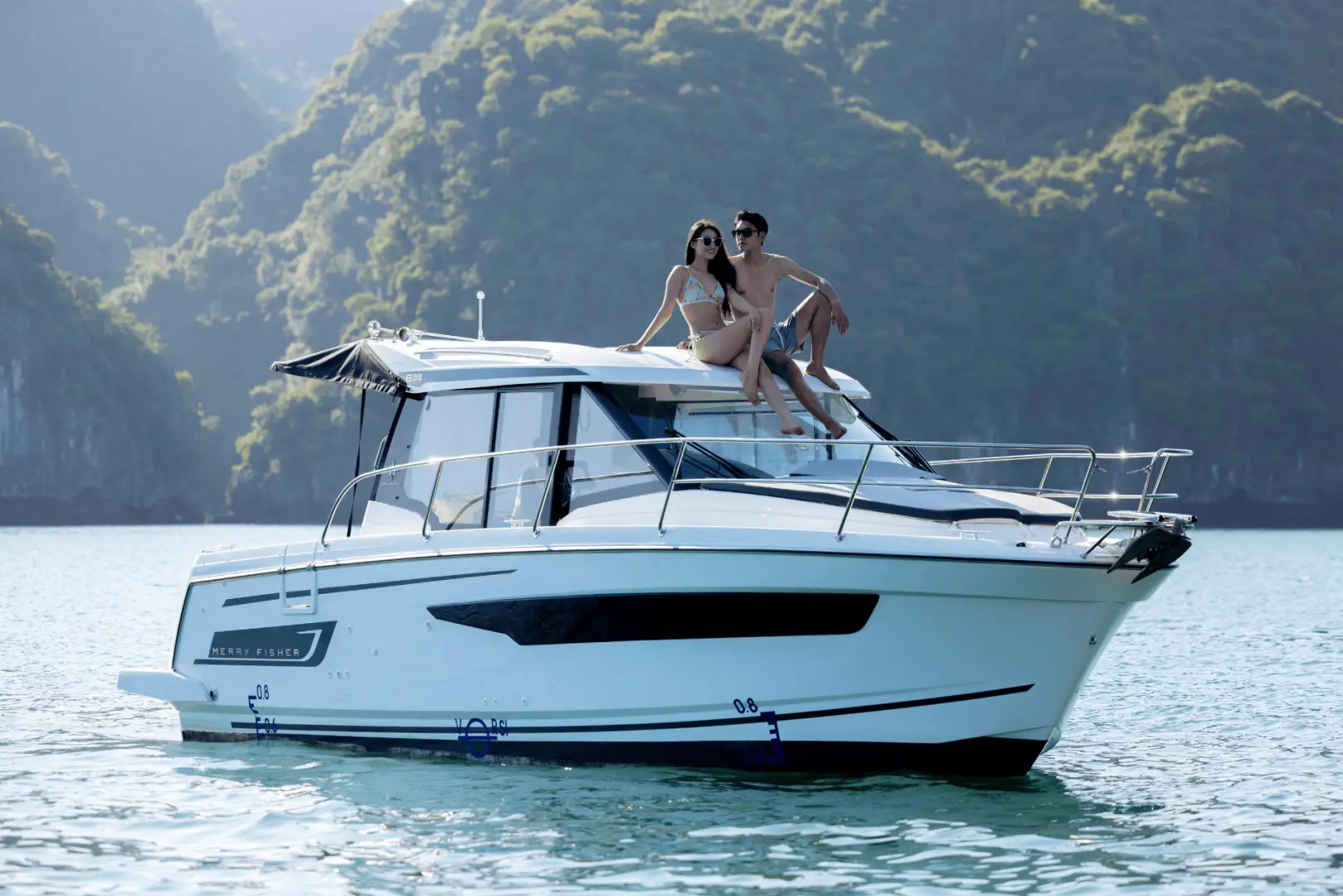 A couple sits together on the roof of a private yacht, enjoying the breathtaking scenery and warm sunshine of Halong Bay.