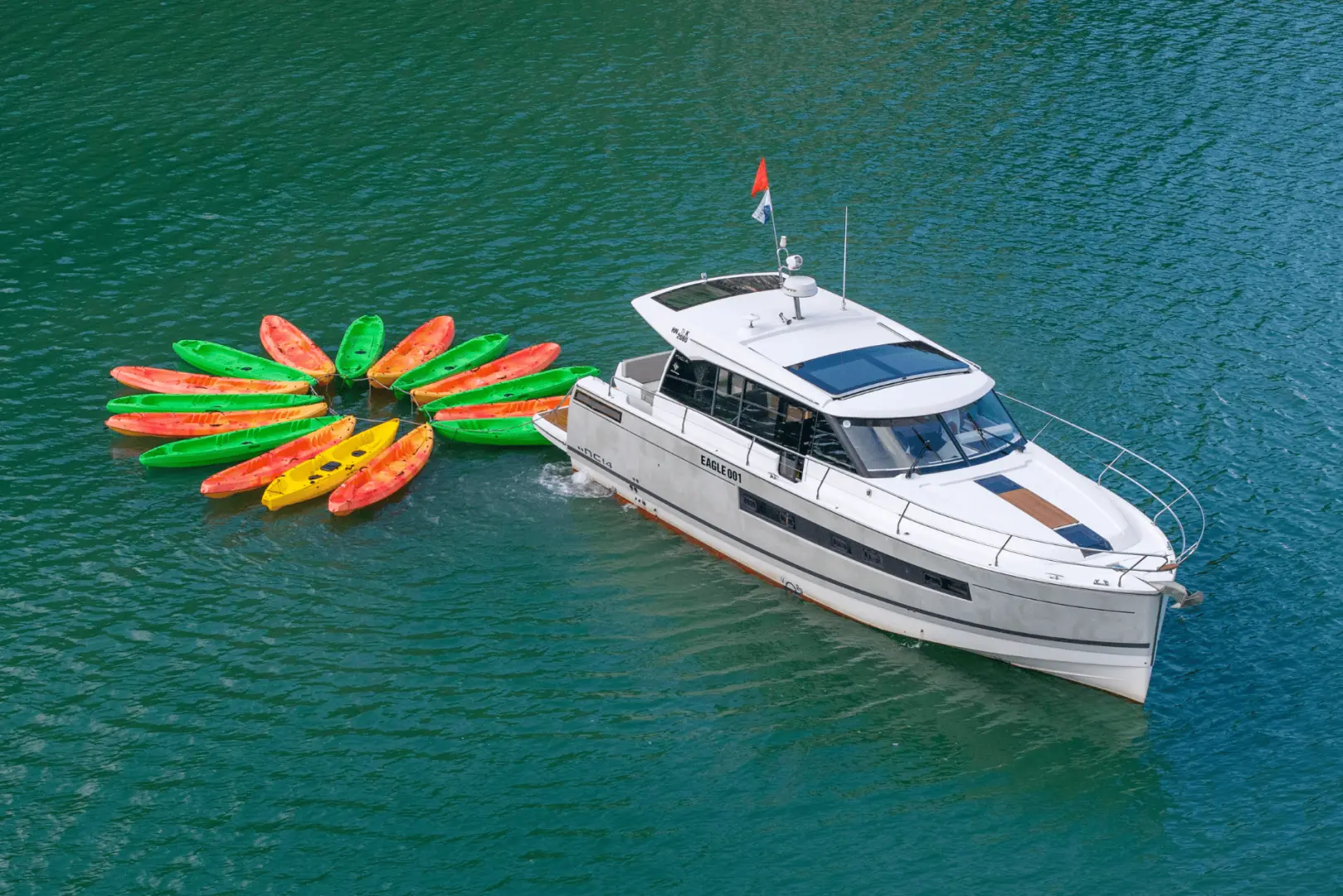 An aerial view of a private yacht anchored in Halong Bay, with a vibrant circle of colorful kayaks tied to its side, surrounded by lush green mountains, perfect for adventure.