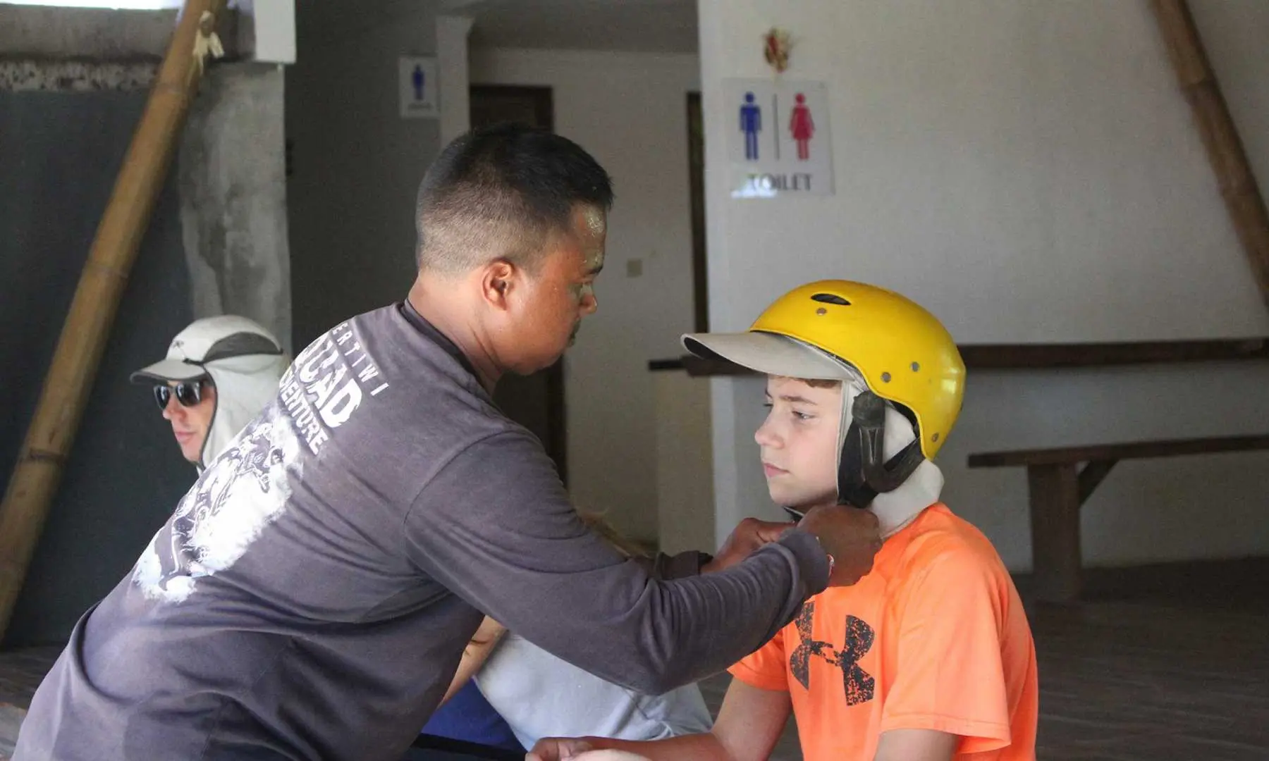 Before the Bali UTV off-road adventure, a professional guide provides personalized safety instruction to a small group participant, assisting a child with helmet and protective gear.