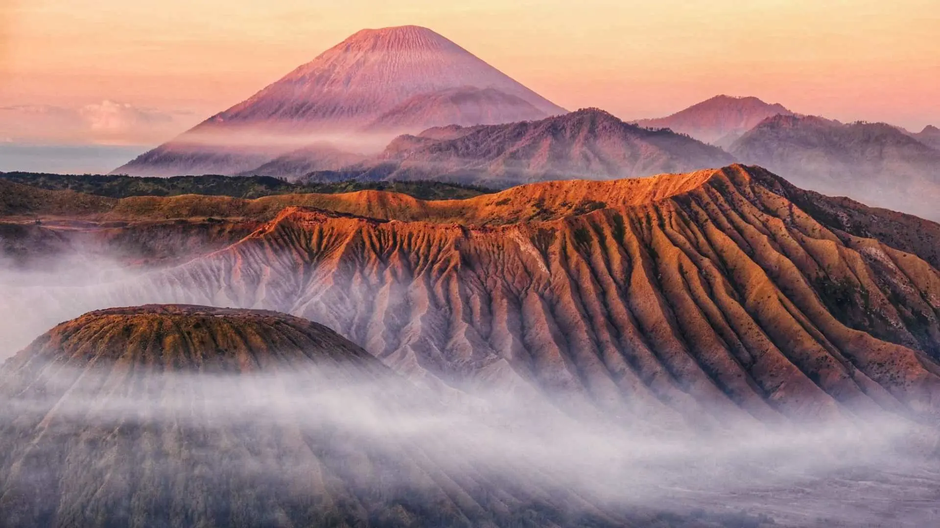 布羅莫火山區的日出美景，晨霧輕柔地籠罩在山谷間，呈現出多層次的火山地貌，氣勢磅礴。