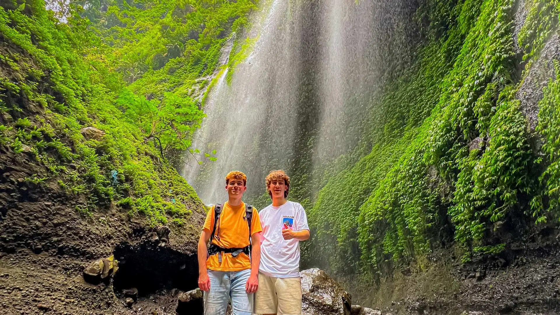 兩位年輕男士在馬達卡里普拉瀑布前開心合影，感受東爪哇熱帶雨林瀑布的壯麗與涼爽。