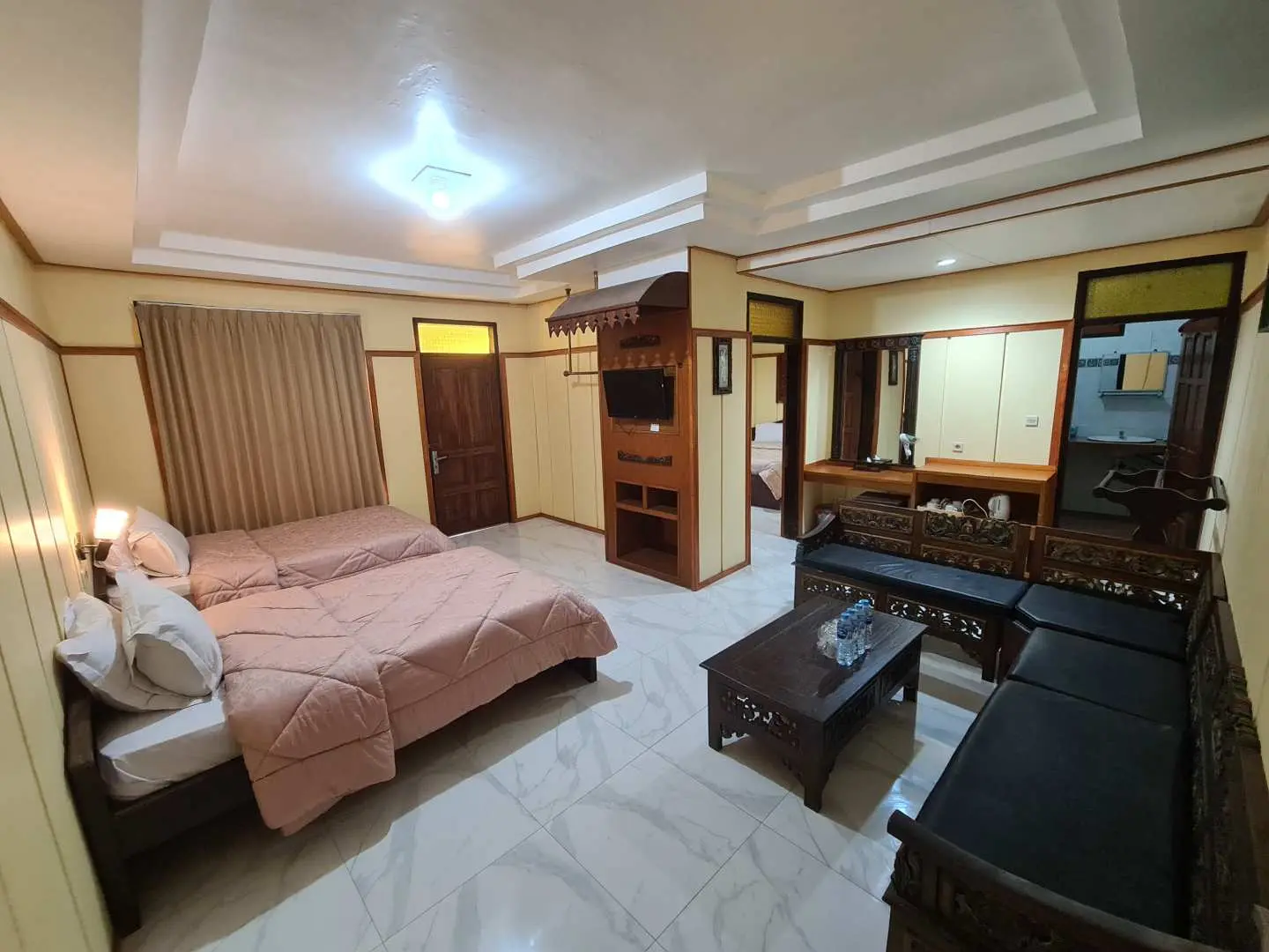 A hotel room with two comfortable single beds and a lounge area, simply decorated with Indonesian local flair, providing a cozy resting space.