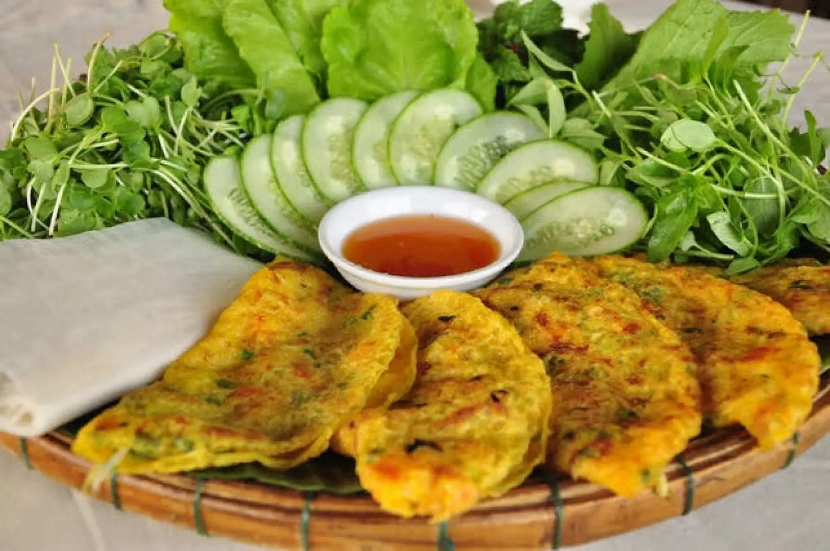 Close-up of delicious Hoi An Banh Xeo (Vietnamese pancakes) served with fresh greens, cucumber, and dipping sauce.