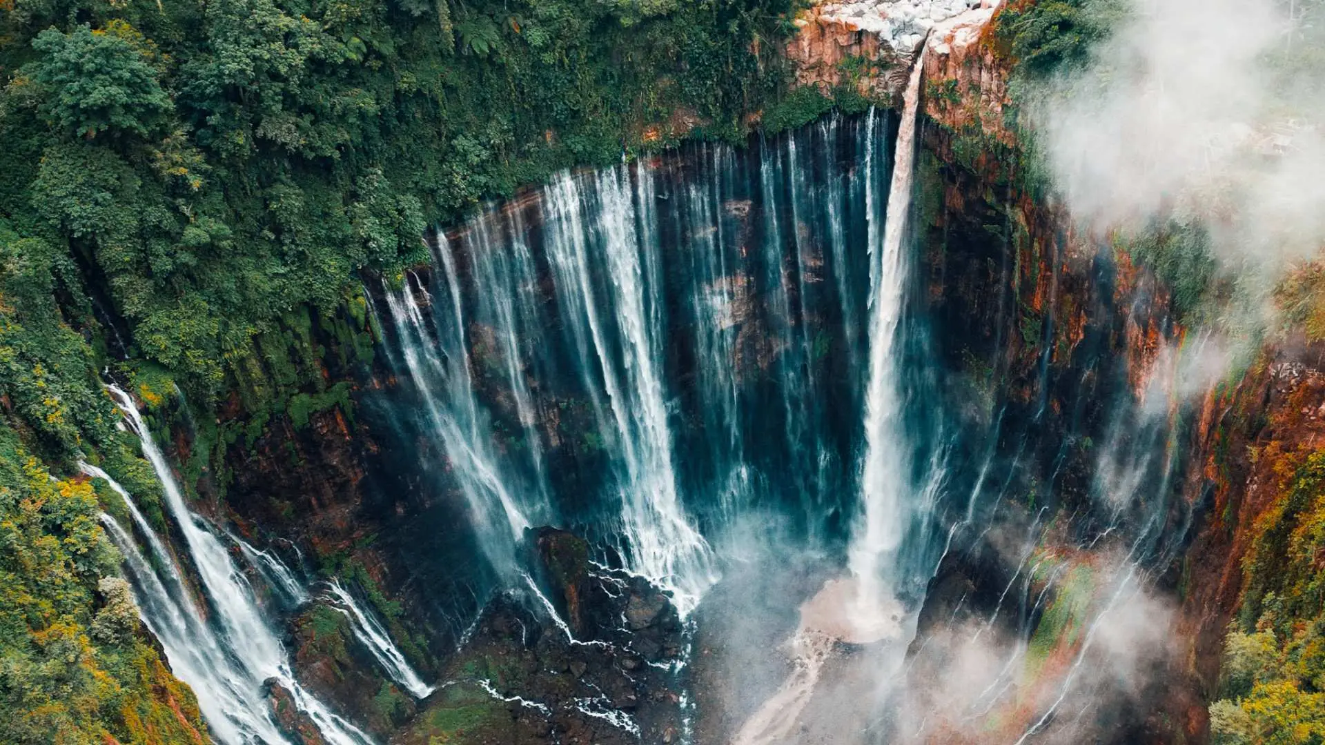 Aerial view of Tumpak Sewu Waterfall in East Java, showcasing multiple majestic streams cascading down lush green cliffs, creating a breathtaking natural wonder.