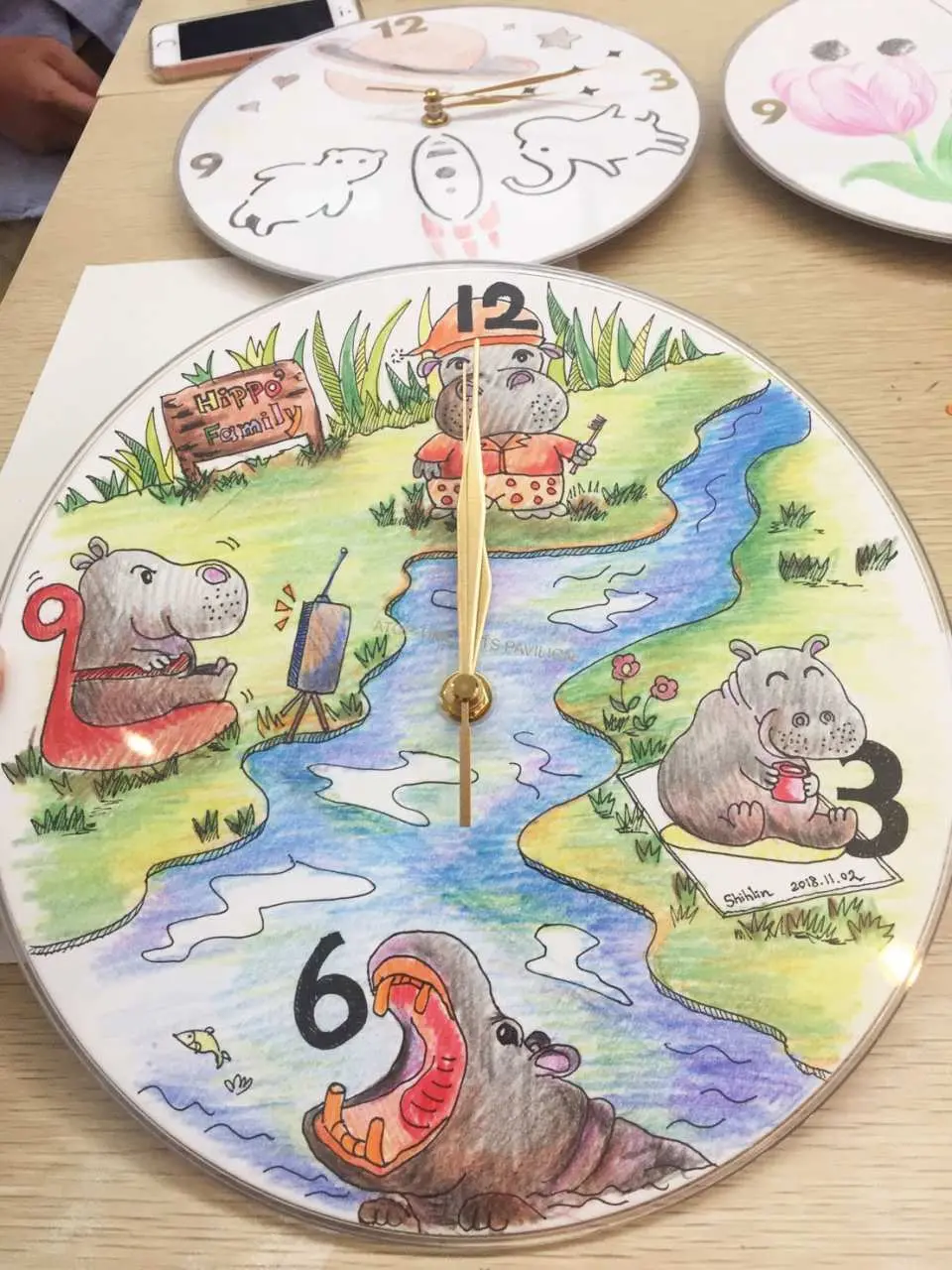 王鼎時間科藝體驗館的彩繪時鐘成品，圓形鐘面上繪製著可愛河馬、河流與數字圖案，展現學員獨特的創意。