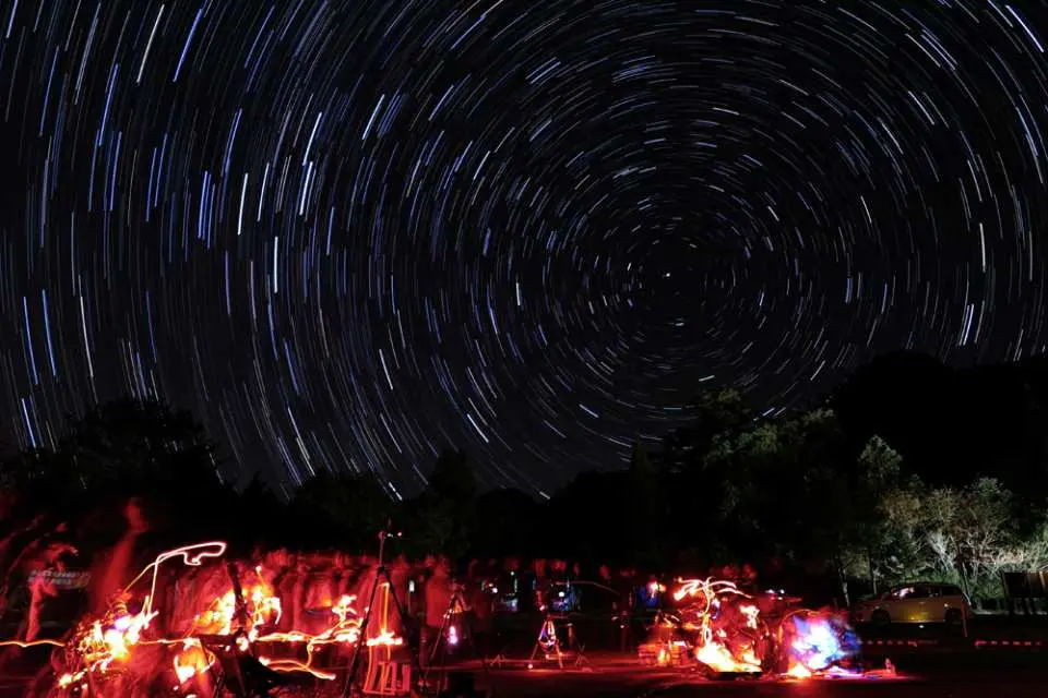 大雪山國家森林遊樂區夜間璀璨星空與星軌，展現夜晚的奇幻景緻，下方人群與燈光勾勒出觀星活動，體驗自然野趣。