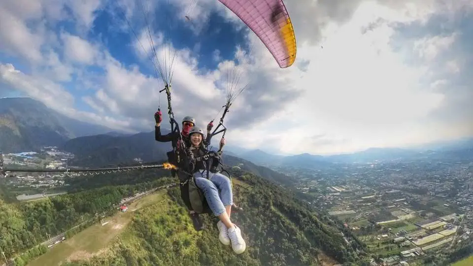 A smiling participant enjoys tandem paragliding with a professional instructor in Nantou Puli, marveling at the panoramic mountain and city views from high above.
