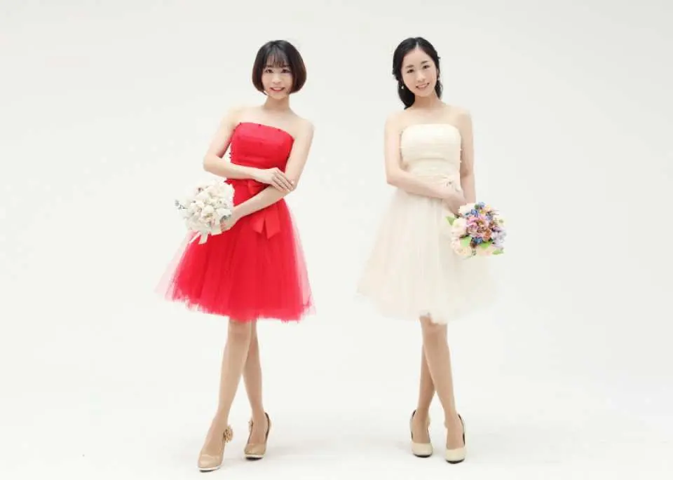 兩位閨蜜在韓國攝影棚穿著活潑的紅色與白色短禮服，手持精緻花束，開心擺拍，展現青春洋溢的友情寫真。