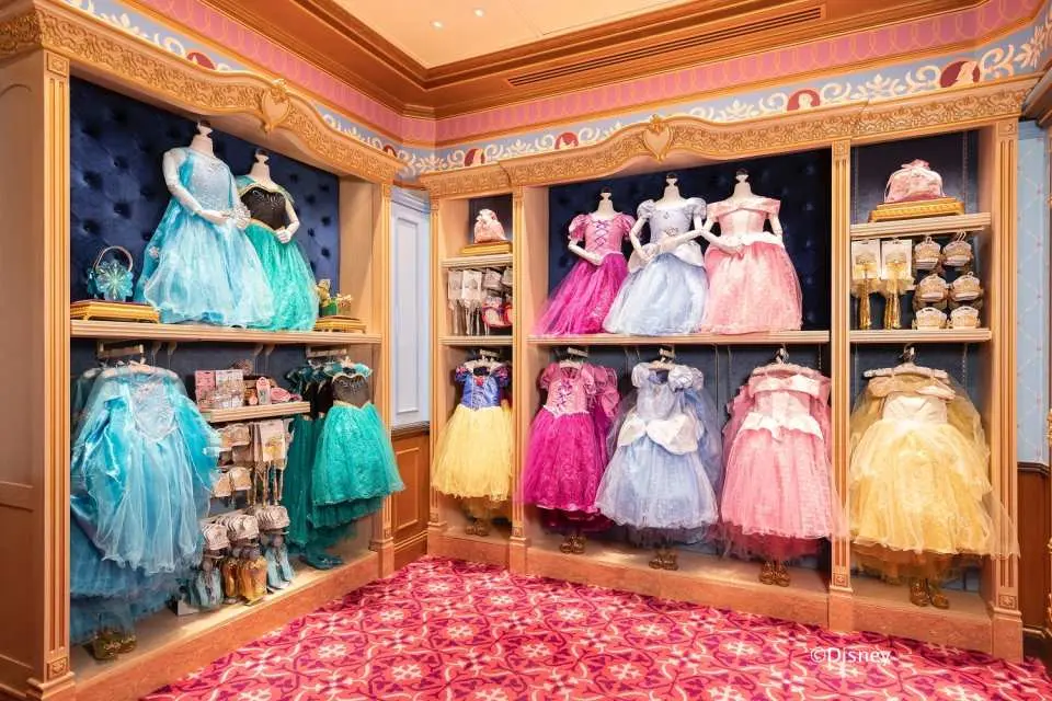 香港迪士尼魔法化妝廳內，牆上展示著多款經典迪士尼公主禮服，如艾莎、安娜、白雪公主等，供小女孩選擇。
