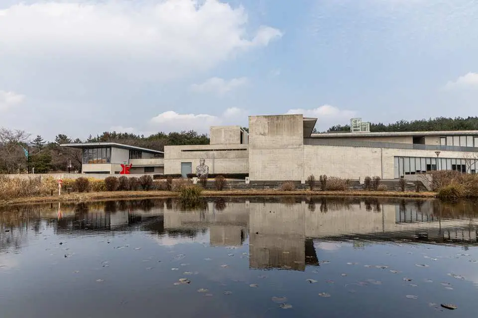 Exterior of Jeju Bonte Museum designed by Ando Tadao, with its minimalist concrete structure reflecting in calm water, showcasing harmony between nature and architecture.