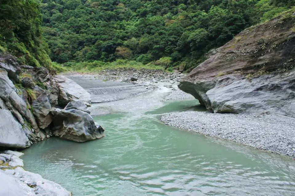 花蓮萬榮野溪溫泉溯溪路線上的壯麗自然風光，清澈碧綠的溪流蜿蜒穿梭於兩旁高聳的峽谷與茂密山林之間，展現台灣原始之美。