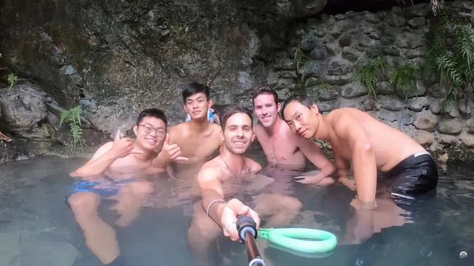 花蓮萬榮野溪溫泉溯溪後，一群男性朋友在摩里沙卡洞穴溫泉中享受放鬆泡湯的時刻，開心地自拍留念，展現愉悅的旅遊體驗。