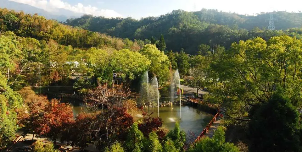 東勢林場湖光山色全景，湖中噴泉與四周紅綠黃相間的樹木，展現台中森林度假的豐富自然風貌。