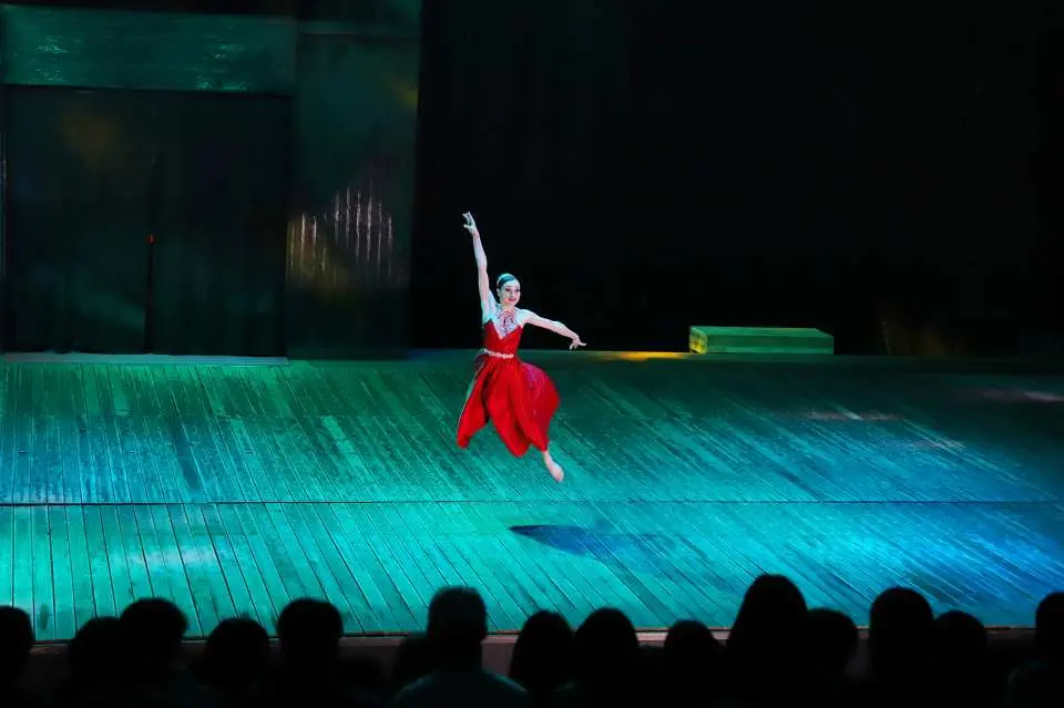 A dancer in a red costume gracefully leaps on the stage of Jeju Island's Sky Water Show, captured from the audience's perspective, highlighting the stunning stage lighting and performance moment.