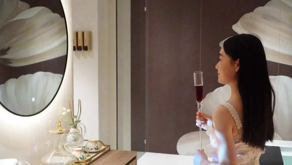 Khách hàng tại Queens Beauty & Spa Hồng Kông trong phòng tắm spa sang trọng, cầm ly rượu vang đỏ, tận hưởng khoảnh khắc thư giãn trước khi ngâm bồn rượu vang hoa hồng.