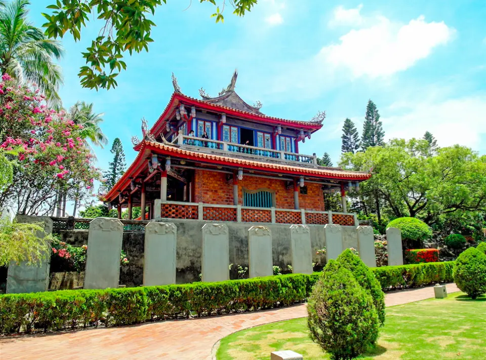 台南赤崁樓全貌，紅瓦飛簷的主建築前方是翠綠草地與整齊步道，右側並列贔屭碑，陽光下展現普羅民遮城作為歷史古蹟的宏偉。