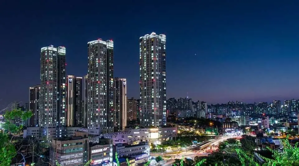 Vibrant night view of Seoul's modern high-rise buildings, illuminated windows, and dynamic car light trails on city roads, reflecting the city's energetic urban charm.