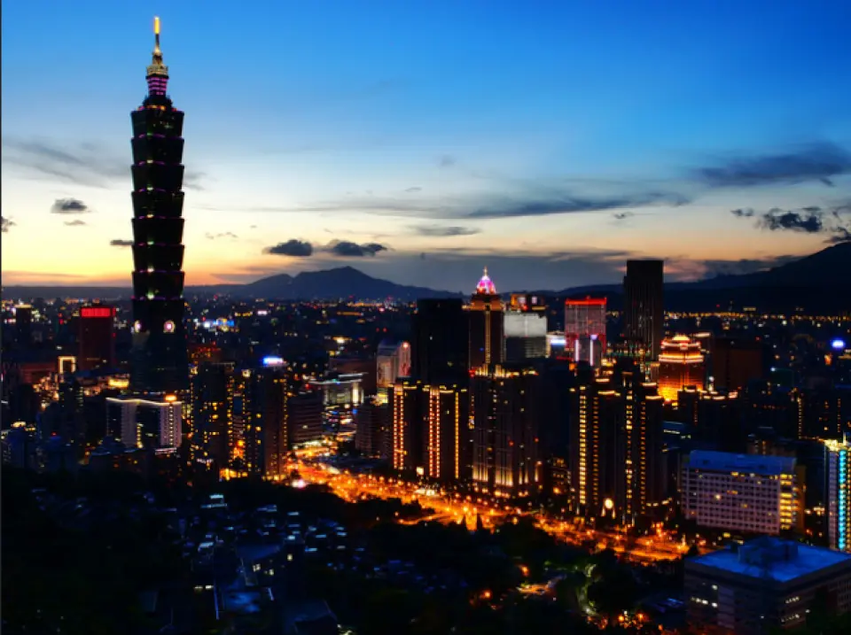 黃昏時分的台北101大樓，與周邊璀璨燈火的城市景觀相互輝映，遠處山巒剪影，展現台北迷人夜色。