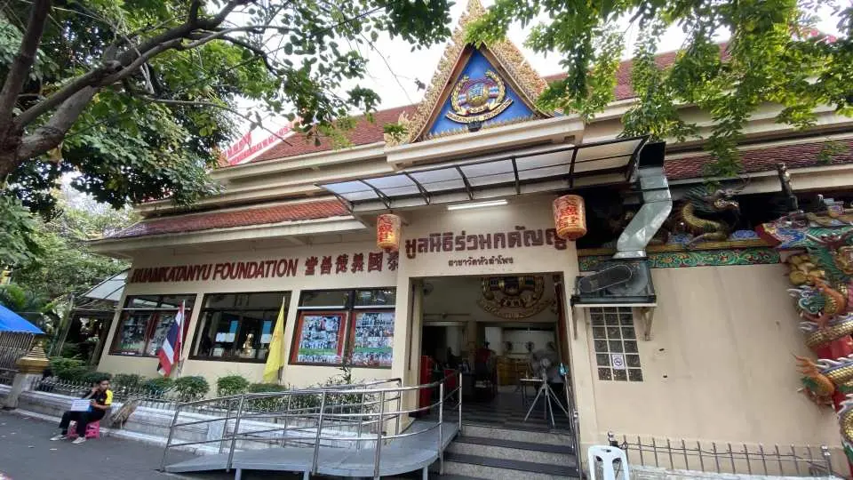The exterior of Bangkok's Ruamkatanyu Foundation, a building blending traditional Thai and Chinese dragon motifs, surrounded by lush trees, an important local charity.