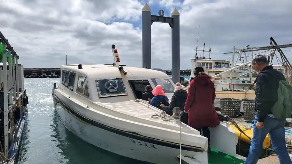 Tourists boarding a small white boat at Penghu's Caiyuan pier, embarking on the short 5-6 minute journey to the Starlight Ocean Ranch's floating platform under a cloudy sky.