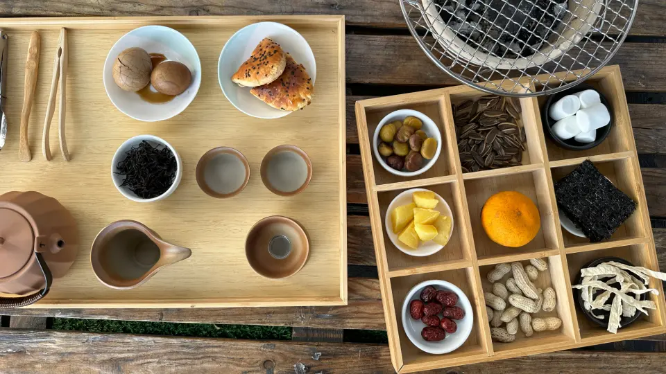 畢瓦客日月潭露營的精緻茶點與烤肉零食組合，包含茶具、茶葉蛋和多種堅果水果點心，豐富湖畔休憩時光。