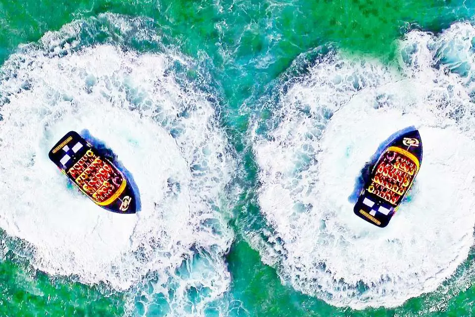 Aerial view of two Gold Coast jet boats performing synchronized high-speed drifts on the emerald Broadwater, creating impressive white splashes. A double thrilling adventure awaits.