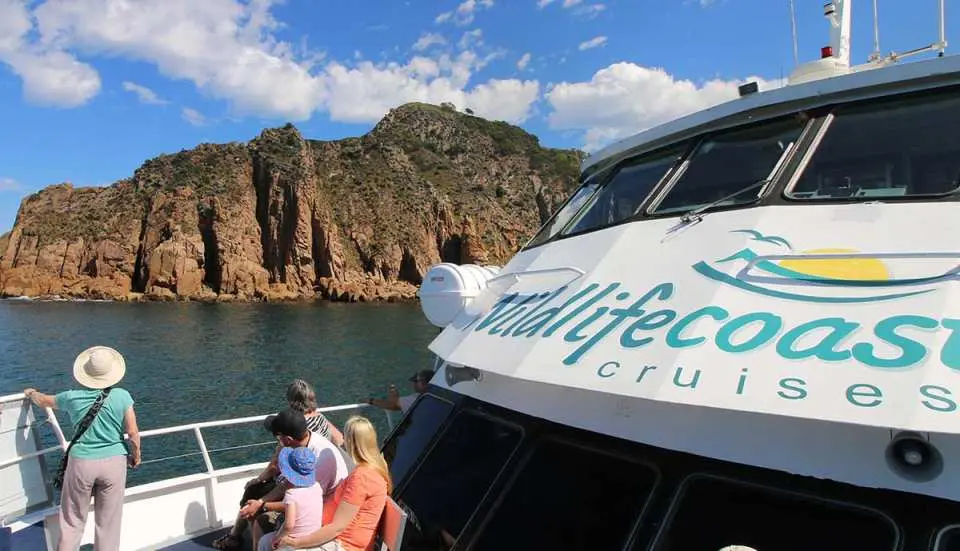 Passengers on a "Wildlife Coast Cruises" boat experiencing the majestic steep granite cliffs and stunning coastline of Cape Woolamai, Phillip Island.