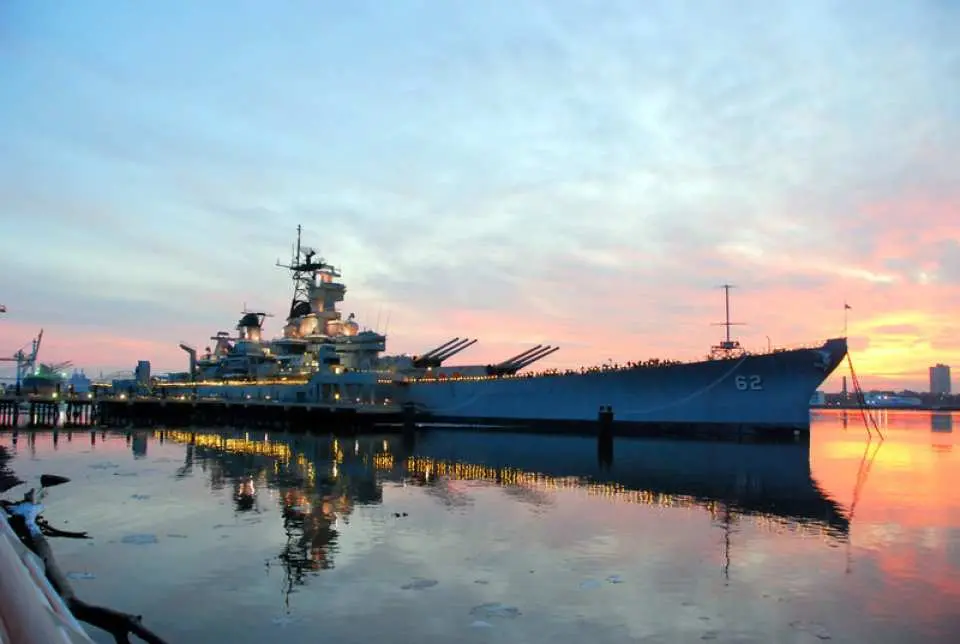 The historic Battleship New Jersey docked majestically in the Philadelphia harbor at sunset, with stunning reflections on the water, a key attraction on the Explorer Pass.