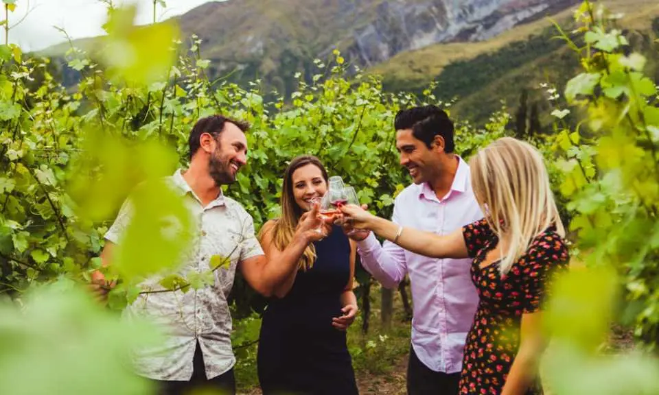 เพื่อนสี่คนกำลังรื่นเริงกับการชิมไวน์ในไร่องุ่น Gibbston Valley ที่ควีนส์ทาวน์ ประเทศนิวซีแลนด์ เพลิดเพลินกับการทัวร์ชิมไวน์สภาพอากาศเย็นที่น่ารื่นรมย์